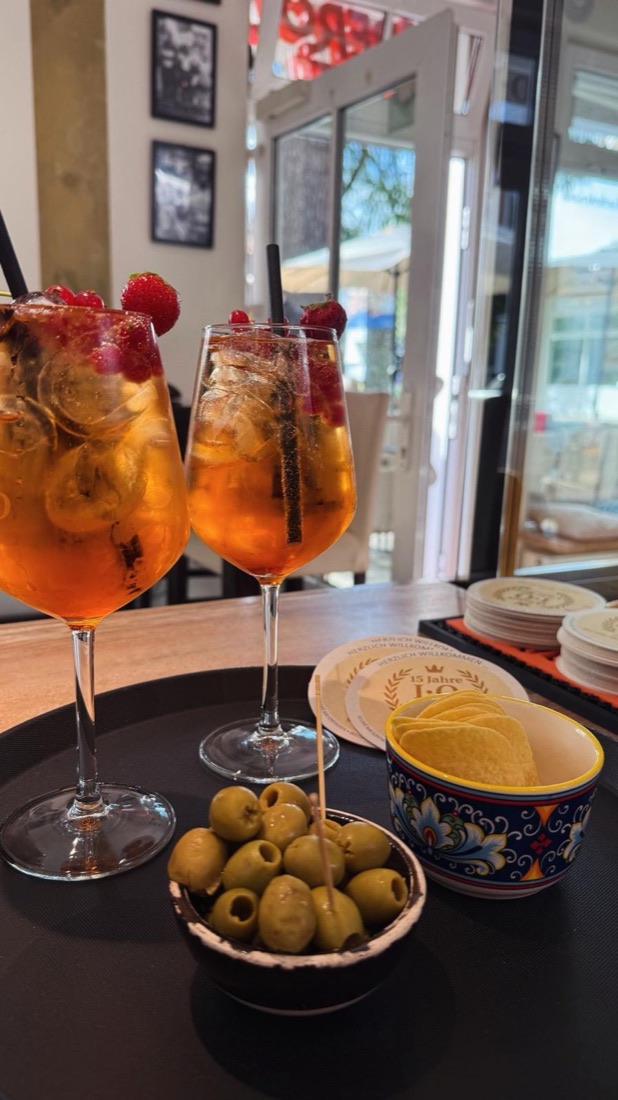 Zwei Spritz mit Beeren, dazu Oliven und Chips